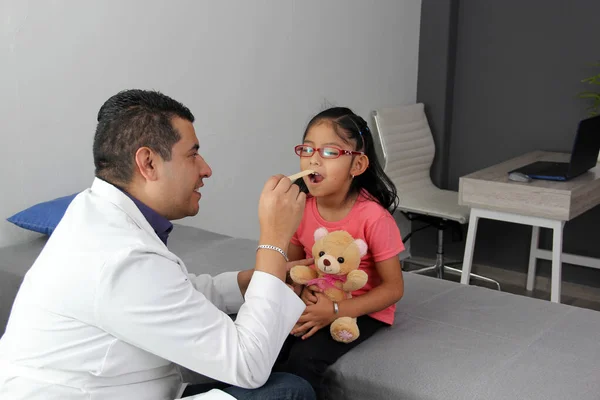 Latino pediatrician doctor checks his girl patient with autism spectrum disorder ASD, he communicates through his teddy bear that he carries as an attachment or transitional object