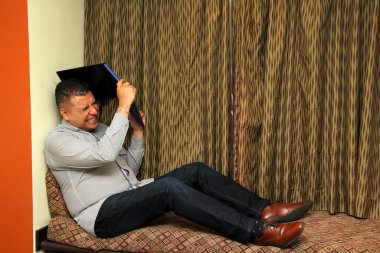 Latino adult man works from his room with his laptop due to overwork, suffers from stress, despair, anger, physical and metal exhaustion, burnout, headache