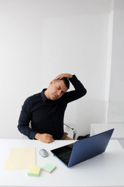 Latino adult man works in his office with his laptop, his head, neck, and back, cervical, lumbar pains due to stress, anxiety and tension