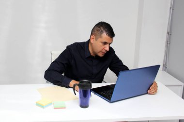 Latino adult man works from his offie with his laptop due to overwork, suffers from stress, despair, anger, physical and metal exhaustion, burnout, headache