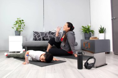 Latin anne ve oğlu su içiyor, su içiyor ve egzersiz yaptıktan sonra müzik dinliyor, yorgun ve mutlu bir şekilde fiziksel aktivitelerini yapıyorlar, aile olarak birlikte kaliteli zaman geçiriyorlar.