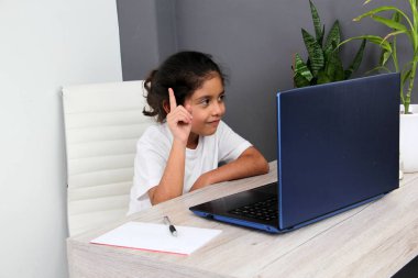 9-year-old Latino girl does home schooling takes online classes at home on a desk with a laptop, studies, is surprised and participates in class