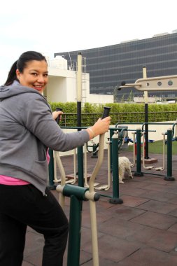 Yetişkin 40 yaşındaki Latin kadın, apartmanının çatı bahçesinde ortak egzersiz ekipmanıyla egzersiz yapıyor.