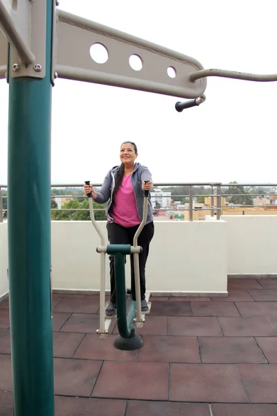 stock image Adult 40-year-old Latina woman exercises on the roof garden of her apartment with shared public exercise equipment