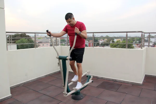 stock image Adult 40-year-old Latino man exercises on the roof garden of her apartment with shared public exercise equipment