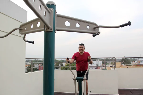 stock image Adult 40-year-old Latino man exercises on the roof garden of her apartment with shared public exercise equipment