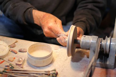 Bir atölyede çalışan, opal taş ve mineralleri parlatarak değerli mücevherler yapan yaşlı bir zanaatkarın elleri.