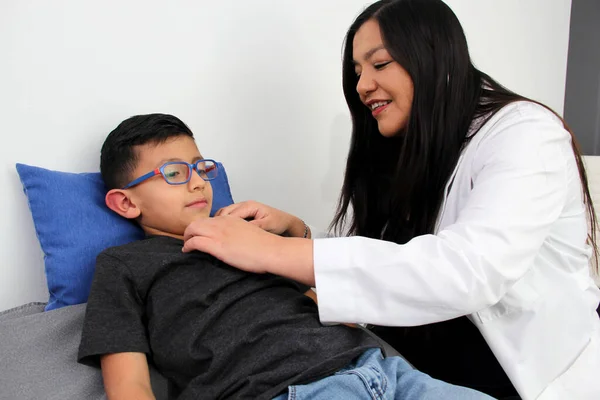 Latina female pediatrician doctor checks her patient 6 year old boy for sore throat from tonsillitis or pharyngitis causing cough