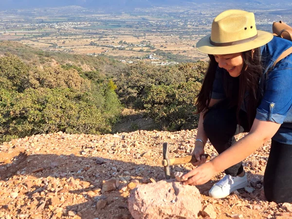 Latina woman with hat and miner\'s pick hammer works as a geologist, studies the composition and structure of the mineral soil of the mountain
