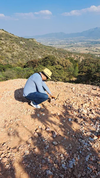 Latin man with hat and miner\'s pick hammer works as a geologist, studies the composition and structure of the mineral soil of the mountain