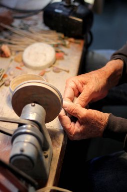 Bir atölyede çalışan, opal taş ve mineralleri parlatarak değerli mücevherler yapan yaşlı bir zanaatkarın elleri.