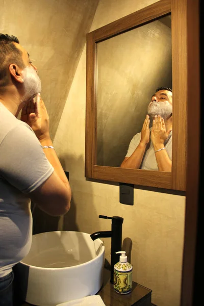 40岁的拉丁裔深色皮肤男子在家里的浴室镜子前刮胡子 因为他害怕打蜡 — 图库照片