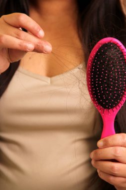 Uzun düz saçları olan Latin yetişkin bir kadın saç dökülmesinden muzdarip. Fırçaya bakıyor. Bir fırçada hastalık yüzünden kaç saç dökülmüş.