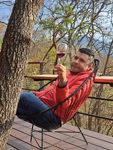 田舎のテラスに座っている黒い髪のラテン系の大人の男は 森のリラックスの真ん中でワインのグラスを楽しんで瞑想します — ストック写真