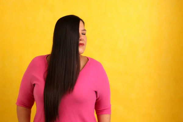 拉丁成年女性穿着粉色毛衣 背景为黄色 有着一头长长的 柔滑的头发 — 图库照片