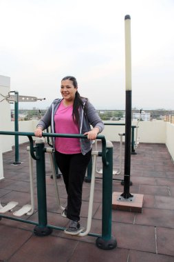 Yetişkin 40 yaşında Latin bir kadın evinin çatısındaki spor salonunda spor yapıyor. Spor aletleriyle.