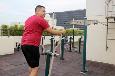 Yetişkin 40 yaşında Latin bir adam evinin çatısındaki spor salonunda spor yapıyor. Spor aletleriyle.
