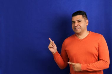 Yetişkin bir adam, 40 yaşında turuncu kazak puanlı Latin esmer. Mavi arka plan, mutlu ve doğal ifadeyle fotokopi alanı.