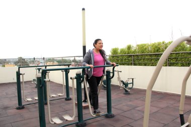 Kırk yaşında yetişkin bir Latin kadın evinin çatı bahçesinde egzersiz yapıyor ve doğum sonrası boş zamanlarından faydalanıyor.