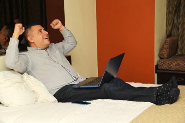 Koyu renk saçlı, 40 yaşında, Latin bir adam laptopuyla ev ofisinin keyfini çıkarıyor.