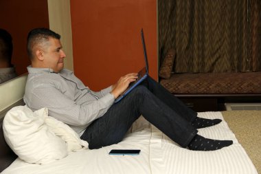 Koyu renk saçlı, 40 yaşında, Latin bir adam laptopuyla ev ofisinin keyfini çıkarıyor.