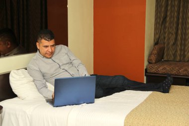 Koyu renk saçlı, 40 yaşında, Latin bir adam laptopuyla ev ofisinin keyfini çıkarıyor.