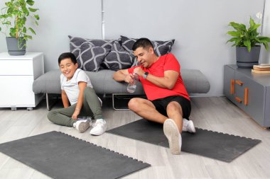 Latin baba ve oğul, evde egzersiz yaptıktan sonra su içmek, su içmek ve enerji sahibi olmak için ara veriyorlar.