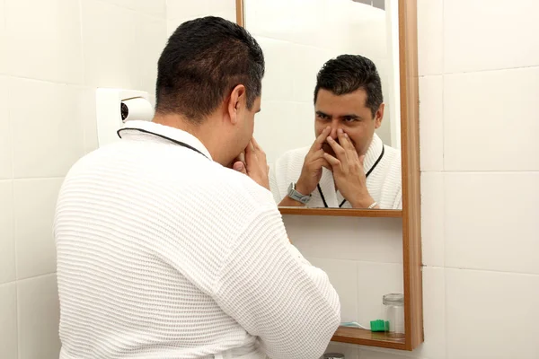 40歳の暗い髪のラテン系男性は 鏡の前で風呂に入った後 健康と新鮮なそれを保つためにクリームで顔の皮膚の世話をします — ストック写真