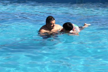 Boşanmış bekar bir baba ve 9 yaşındaki siyah saçlı bir çocuk havuzda birlikte yüzüyor yaz tatilinde ailece vakit geçiriyorlar.