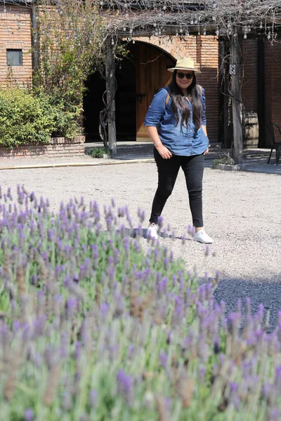 Latin adult woman walks relaxed and calm enjoys walk outdoors with sunglasses and hat in her lavender garden