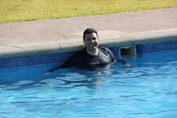 40代のラテン系の男性は 太陽の損傷から身を守るためにシャツで水着を着て夏休みにリラックスするプールを楽しんでいます — ストック写真