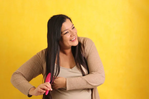 40-year-old Latina woman brushes her straight hair with difficulty because it is already too long