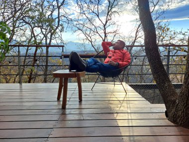 Koyu renk saçlı, 40 yaşında Latin bir adam hafta sonu tatillerinde boş zamanlarında ormanın terasında bir bardak şarap içer.