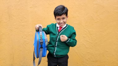 Koyu renk saçlı 9 yaşındaki okul üniformalı Latin çocuk okula geri getireceği yeni beslenme çantasını gösteriyor.