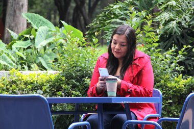 40 yaşında Latin bir kadın cep telefonuyla video görüşmesi yapıyor, internetten alışveriş yapıyor, randevularını alıyor ve açık hava bankında ödeme yapıyor.