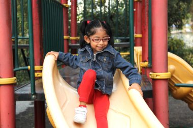 4 yaşındaki esmer Latin kız parkta kaydırağın üzerinde oynuyor. Yoksulluk ve mutluluk içinde yaşıyor.
