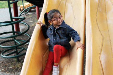 4 yaşındaki esmer Latin kız parkta kaydırağın üzerinde oynuyor. Yoksulluk ve mutluluk içinde yaşıyor.