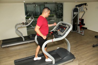 Koyu renk saçlı Latin yetişkin adam, diyabet ve hipertansiyondan kaçınmak için spor salonunda koşu bandında egzersiz yapıyor.