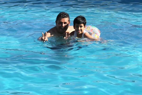 Divorced single dad and 9-year-old black-haired Latino son swim in pool together spend quality family time on summer vacation