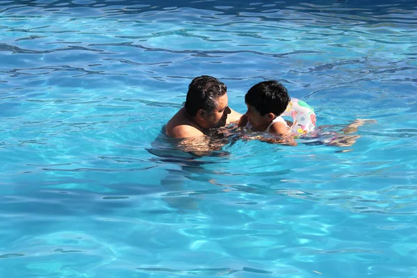 Divorced single dad and 9-year-old black-haired Latino son swim in pool together spend quality family time on summer vacation
