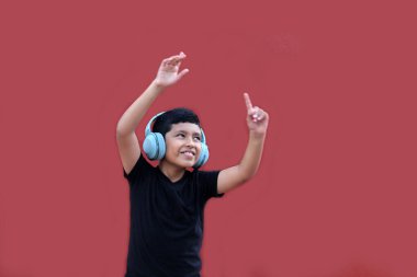 9 yaşındaki esmer tenli Latin çocuk kulaklıklarını dinliyor ve heyecanlı ve mutlu bir şekilde dans ederken müzik dinliyor.
