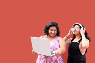 20 yaşındaki iki genç Latin esmer kadın ders çalışmak ve müzik videoları izlemek için dizüstü bilgisayar ve kulaklık kullanıyor.