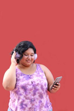 20 yaşındaki genç esmer ve şişman kadın müzik dinlemek için kulaklık kullanıyor, müzik listesi, podcastlar, sesli kitaplar.