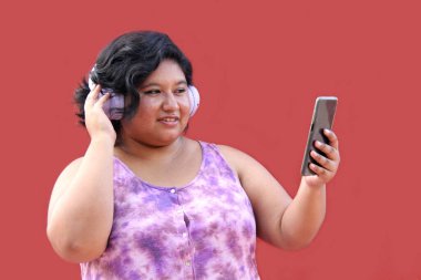 20 yaşındaki genç esmer ve şişman kadın müzik dinlemek için kulaklık kullanıyor, müzik listesi, podcastlar, sesli kitaplar.