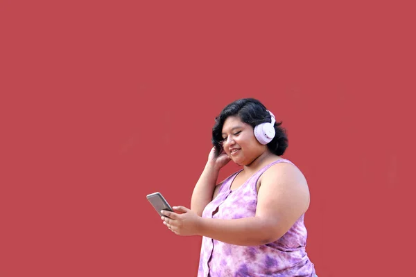 Young 20-year-old brunette and fat woman uses headphones connected to her cell phone to listen to music, playlists, podcasts, audiobooks