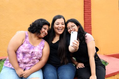 Genç anne ve Latin kızları selfie çekmek ve video görüşmeleri yapmak için cep telefonu kullanıyor.
