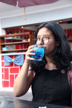 Genç esmer Latin kadın mavi renkli Azulito alkollü bir içecek içiyor votka, biber tozu enerji içeceği sağlığa zararlı.