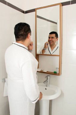 Esmer tenli 40 yaşındaki Latin adam diş dökülmesini ve çürükleri önlemek için banyo aynasının önünde dişlerini fırçalıyor.