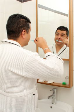 Esmer tenli 40 yaşındaki Latin adam diş dökülmesini ve çürükleri önlemek için banyo aynasının önünde dişlerini fırçalıyor.