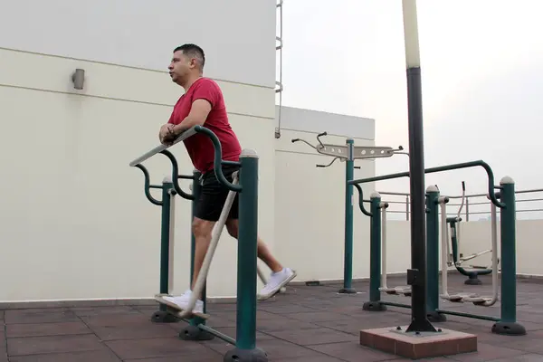 Dark-haired 40-year-old Latino man exercises on the roof garden of his apartment building to prevent overweight, diabetes and hypertension